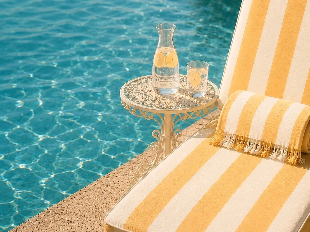 A striped lounge chair beside a sparkling pool with a carafe of lemon water